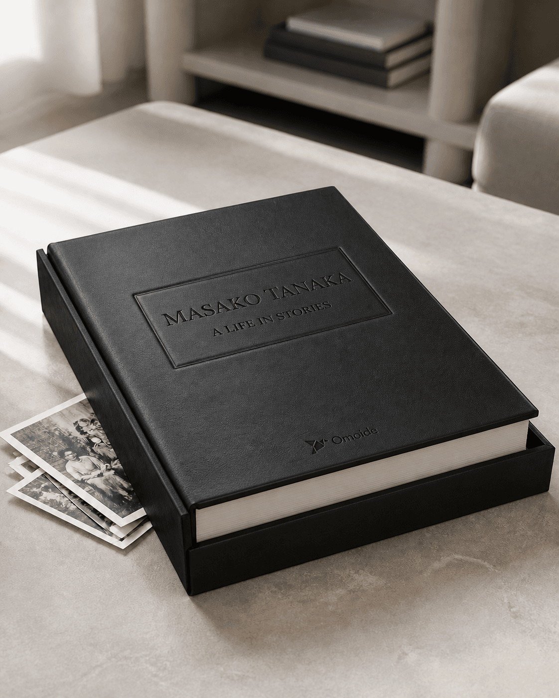 Design preview of a personalized Omoide biography for Masako Tanaka, bound in black leather and resting on a family coffee table.